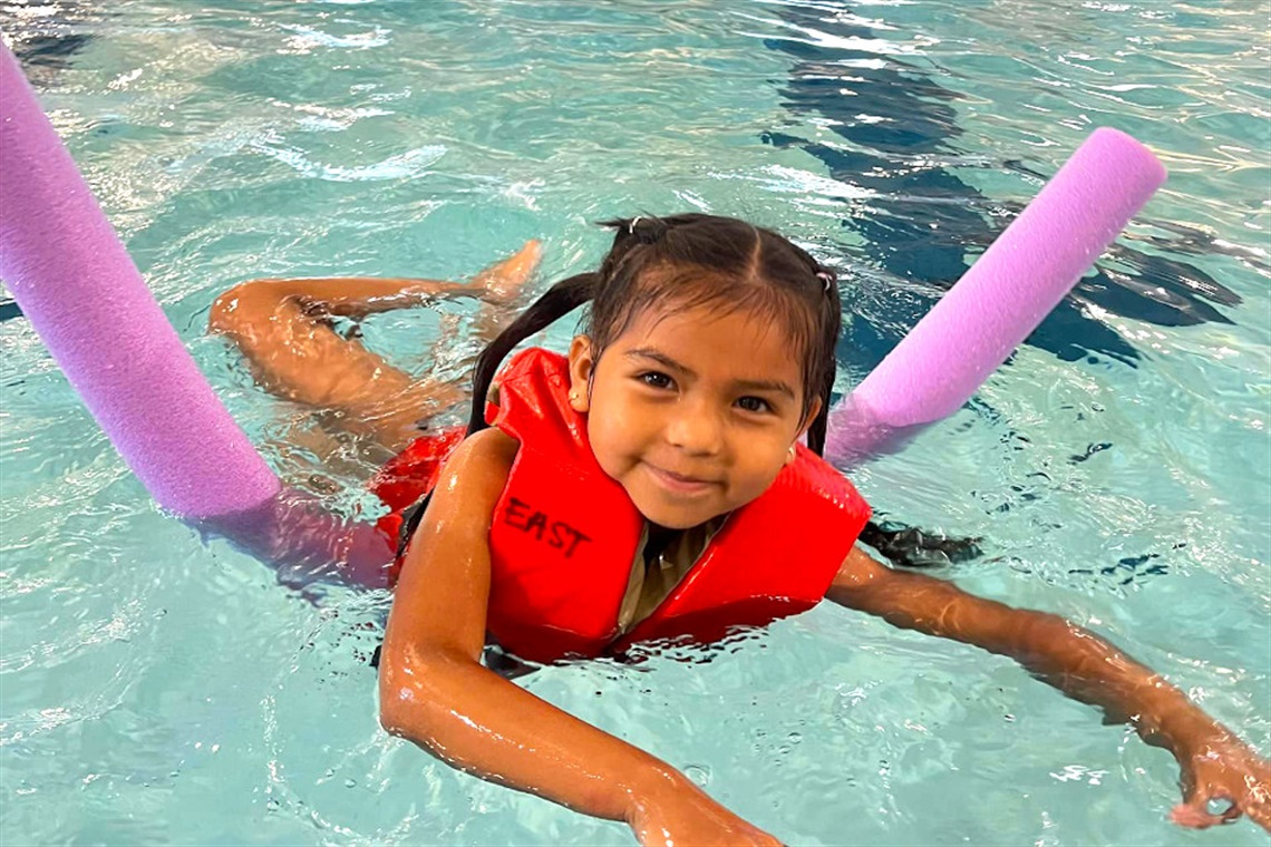 Girl swimming in pool with purple noodle floatie.