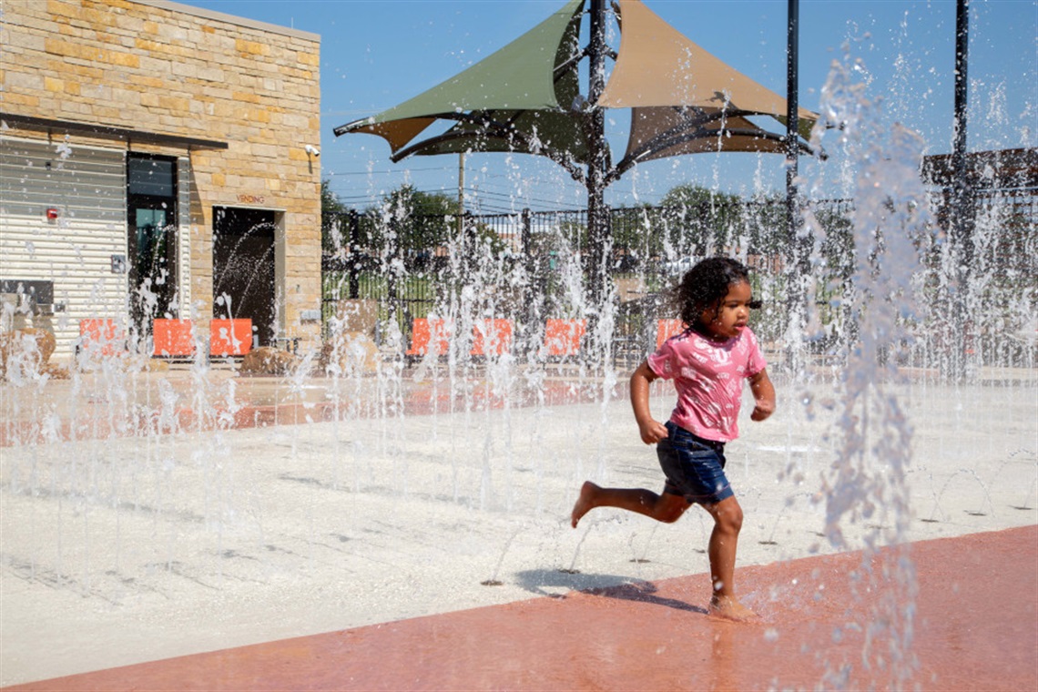 Young girl running through spraying water jets at splash pad