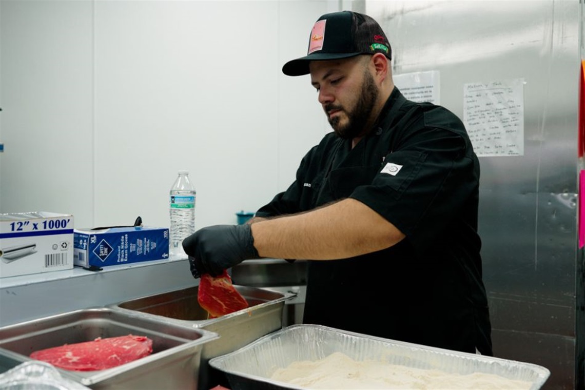 A chef wearing a black uniform and a cap preparing food in a commercial kitchen.
