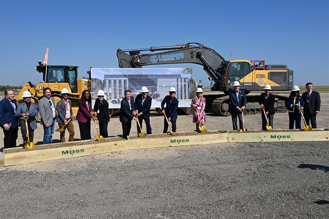 People lined up in a bulldozer holding golden shovels to break ground