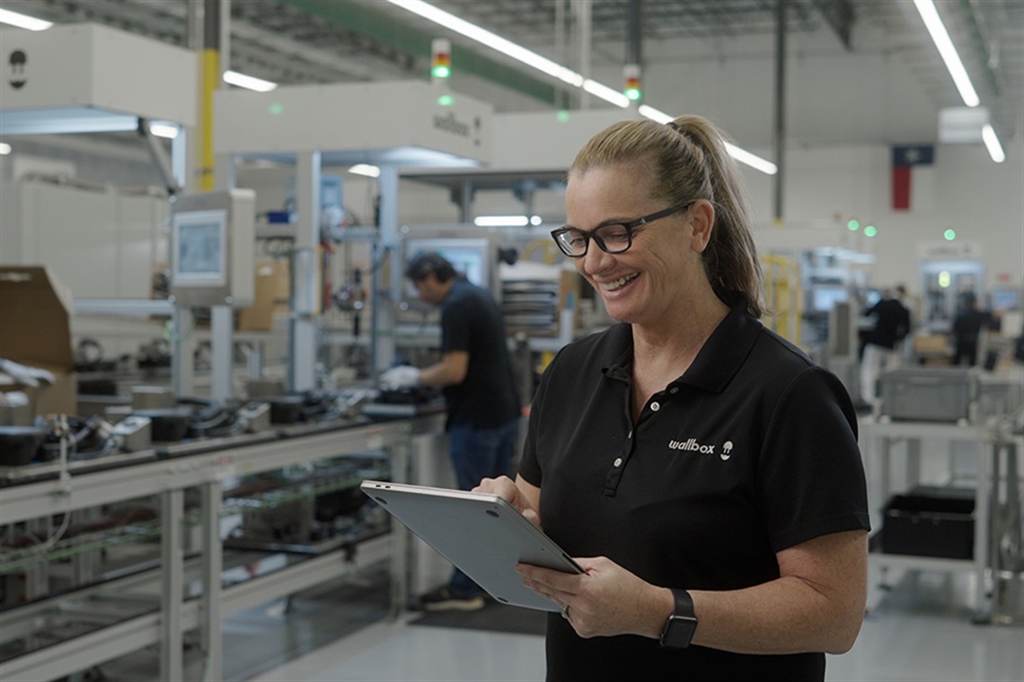 Woman in a manufacturing facility looking at an ipad and smiling