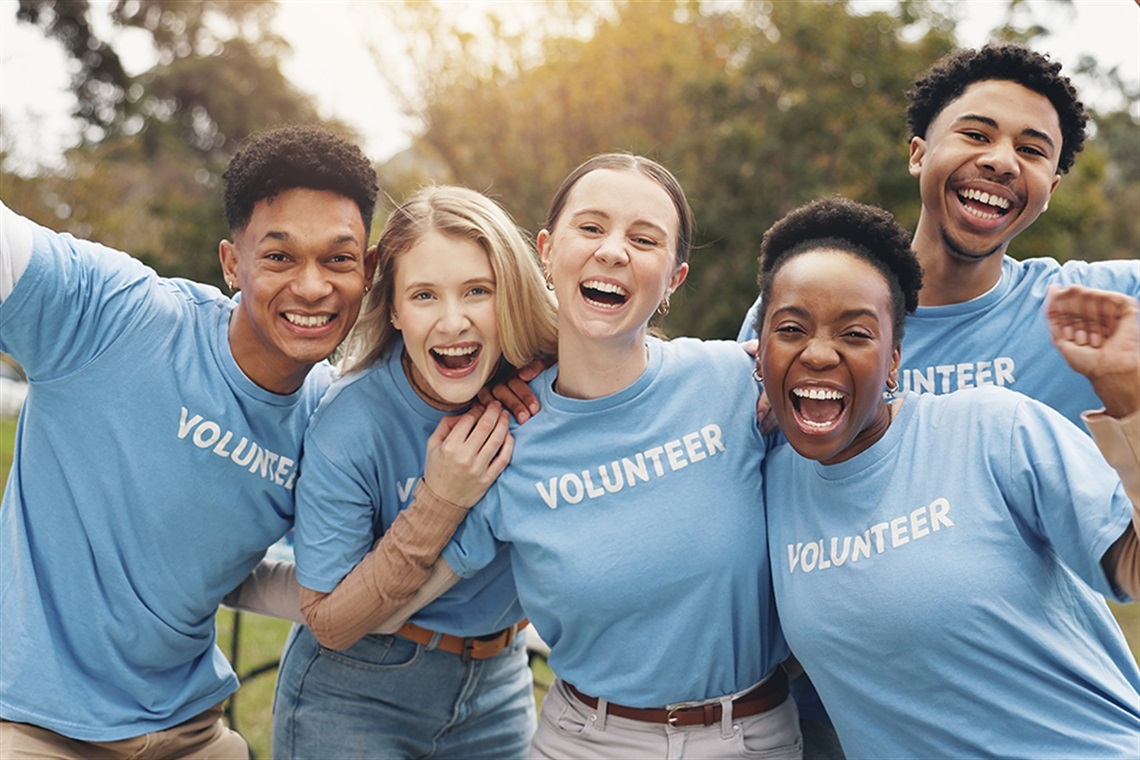 Group of smiling adults wearing blue T-shirts that read Volunteer on them in white type.
