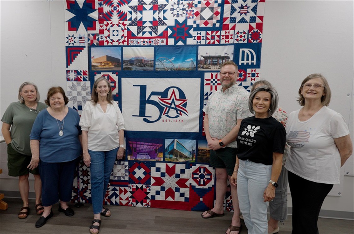Members of the Quilters Guild of Arlington posing for photo around the Arlington 150th Commemorative Quilt.