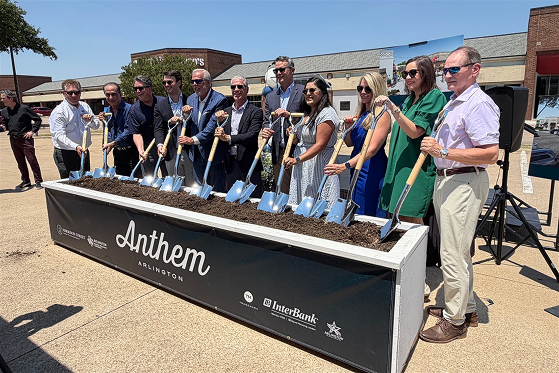 A group of people smiling holding shovels over a planter of dirt with 