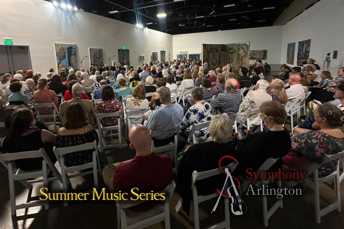 Audience seated in a large room with artworks on the walls, attending a 