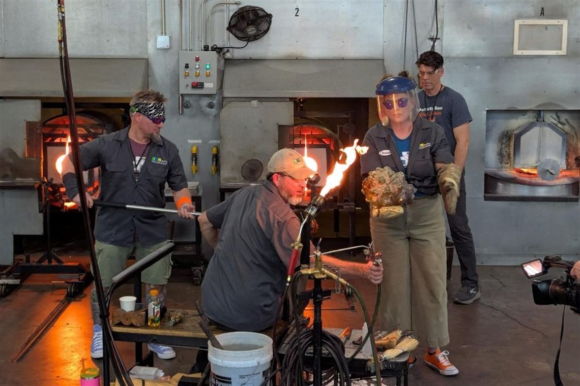 Four people with a blow torch blowing glass in an industrial space 