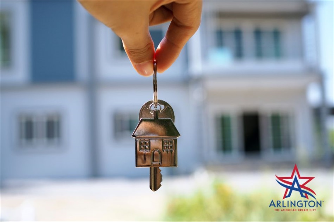 A pair of keys being dangled in front of a white home.