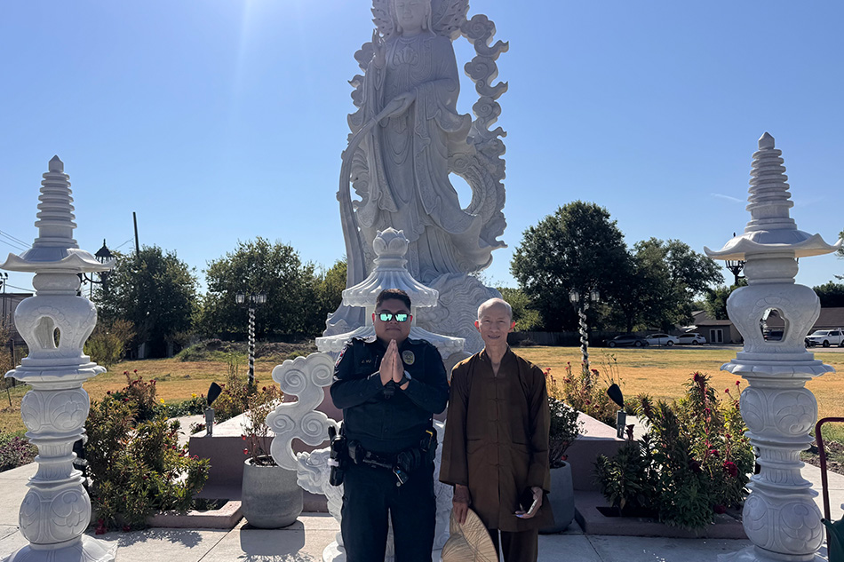 A police officer and community member posing in front of a Buddhist statue