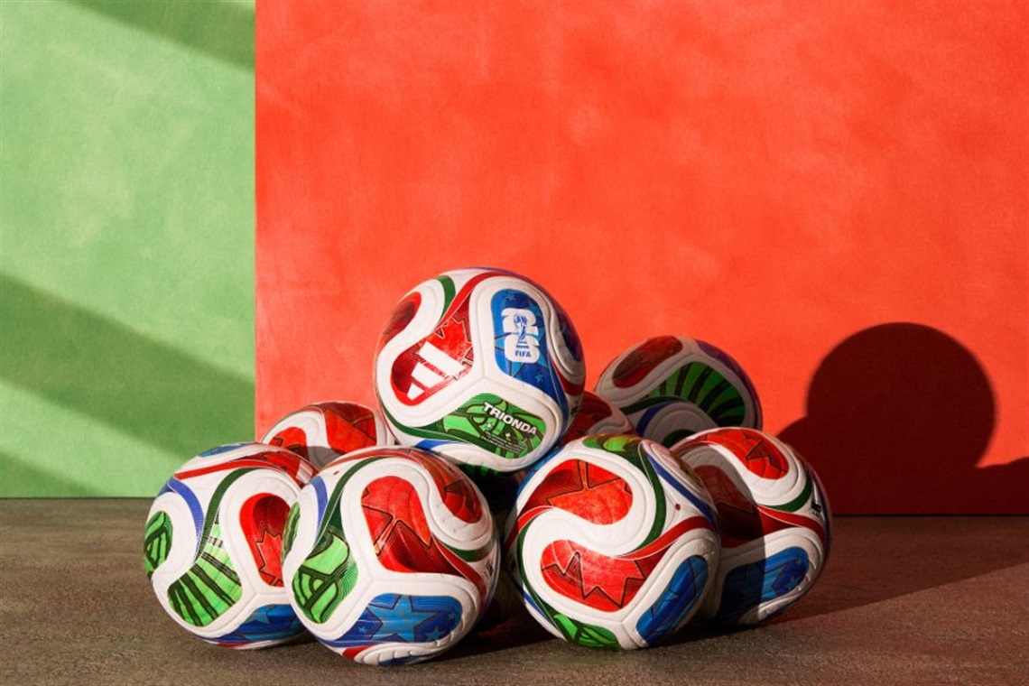 A collection of colorful Adidas soccer balls stacked against a red and green background.