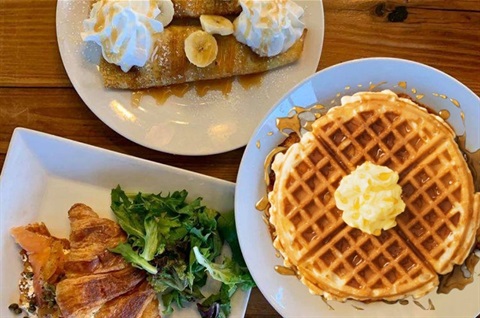 breakfast waffles, bacon and crepes on plates.