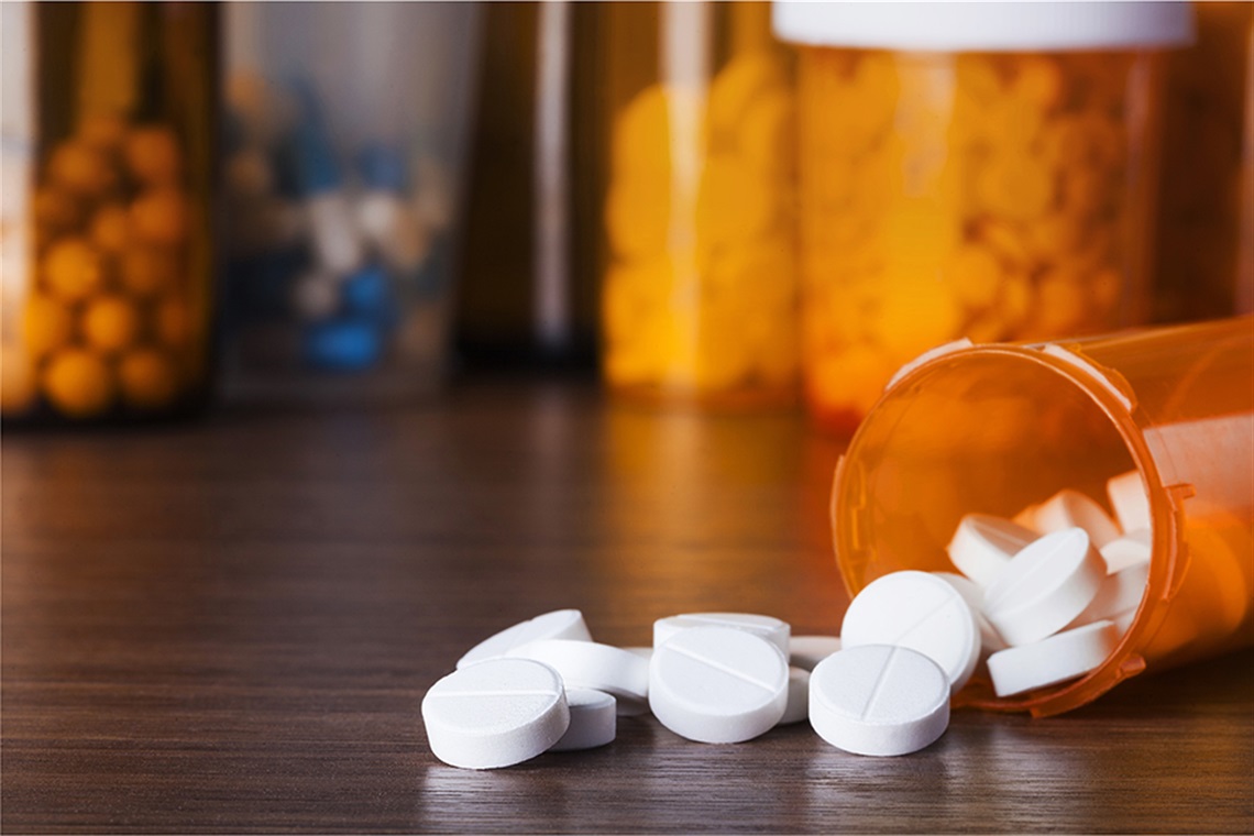 Pills outside of a pill bottle in the foreground with four pill bottles pull of pills in the background.