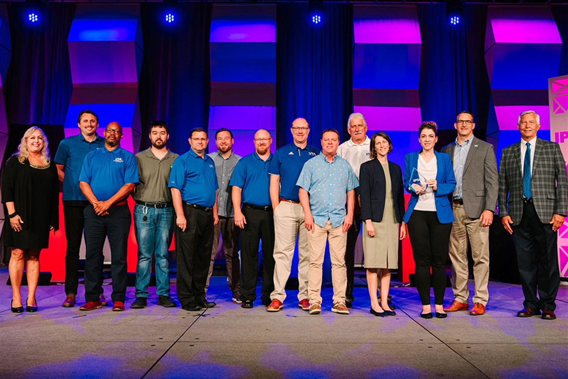 Group of people standing on stage looking at the camera.  UTA received an Award of Excellence for Innovation from the International parking & Mobility Institute (IPMI)