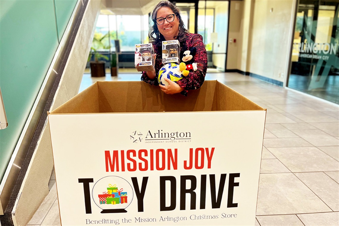 Woman holding toys in front of toy collection box. 