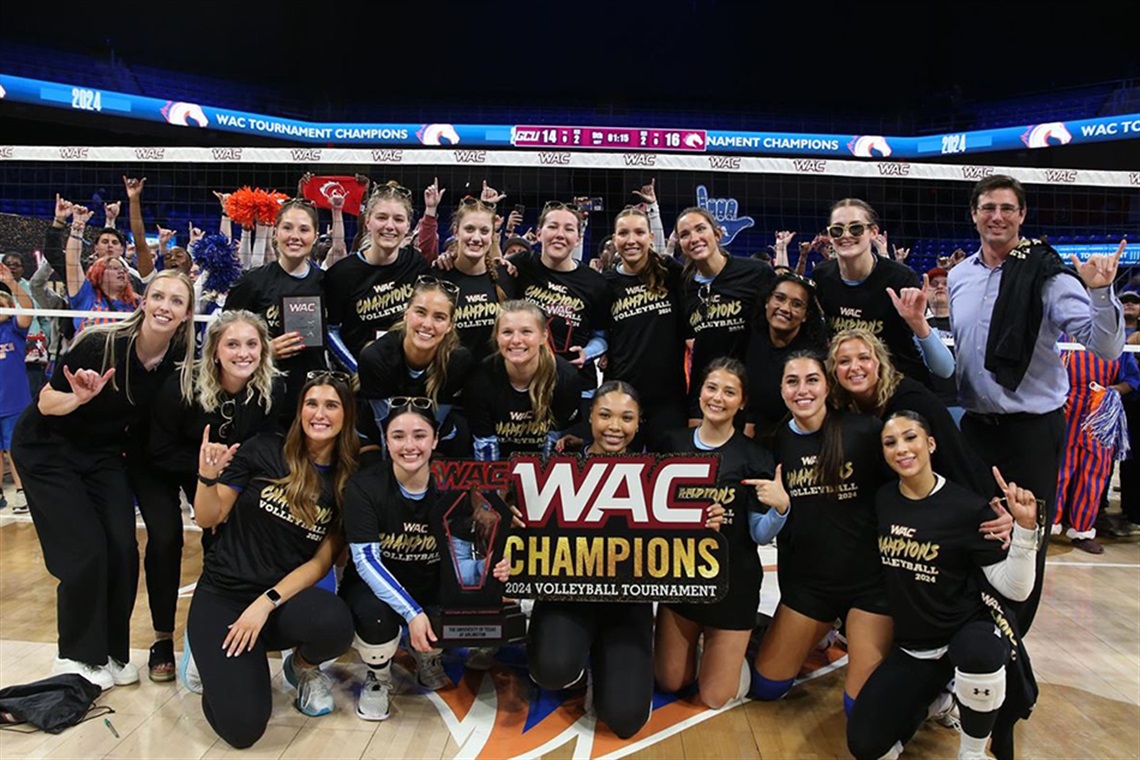 Members of the UT Arlington volleyball team posing for photo with WAC Championship banner.