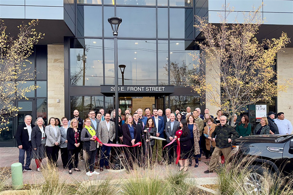 Group of people celebrating ribbon-cutting in front of SFC headquarters building