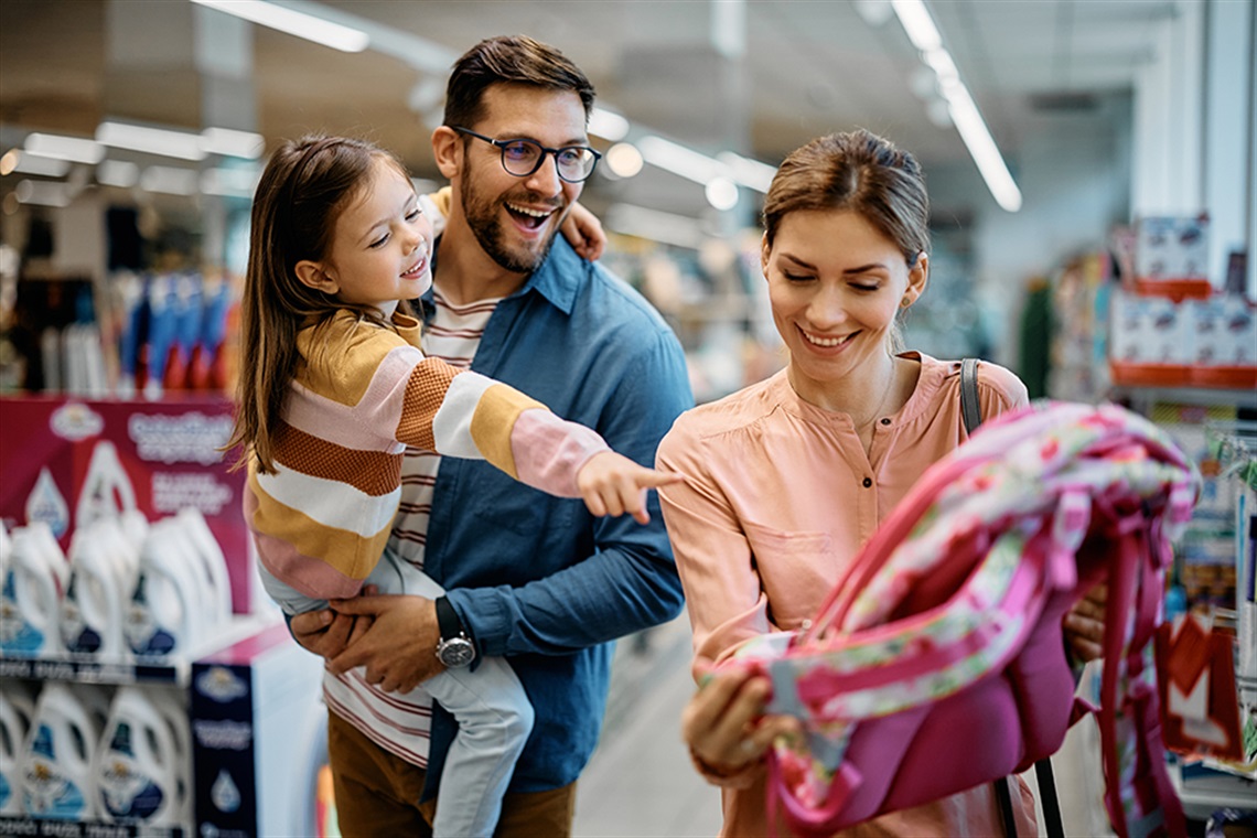 Happy little girl pointing at backpack while buying school supplies with her parents in supermarket. Happy little girl pointing at backpack while buying school supplies with her parents in supermarket.