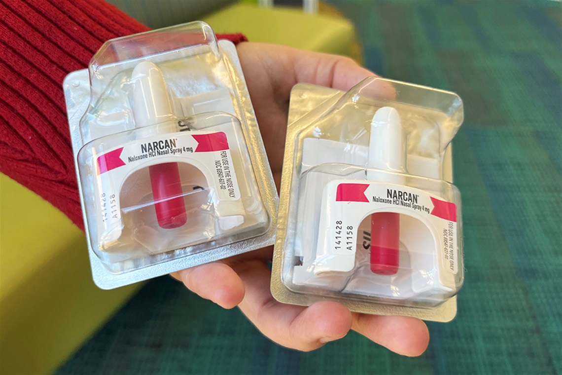 Image of a hand holding two bottles of nasal spray naloxone.