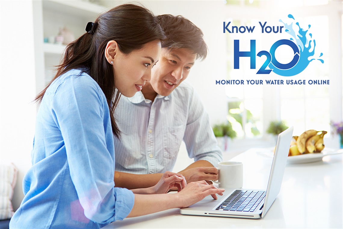 Woman typing on laptop with man standing nearby looking at laptop screen.