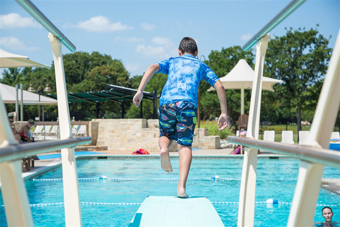 Boy in blue swim suit jumping off diving board