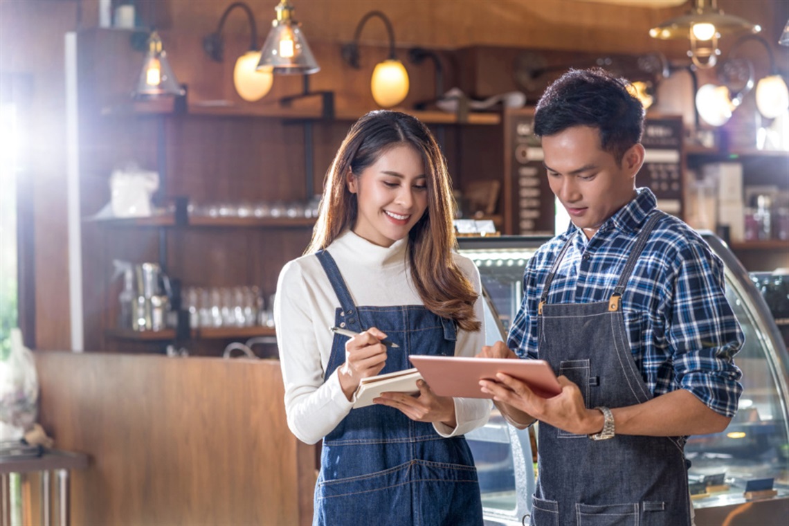 A young woman and man working on a tablet inside a cafe.