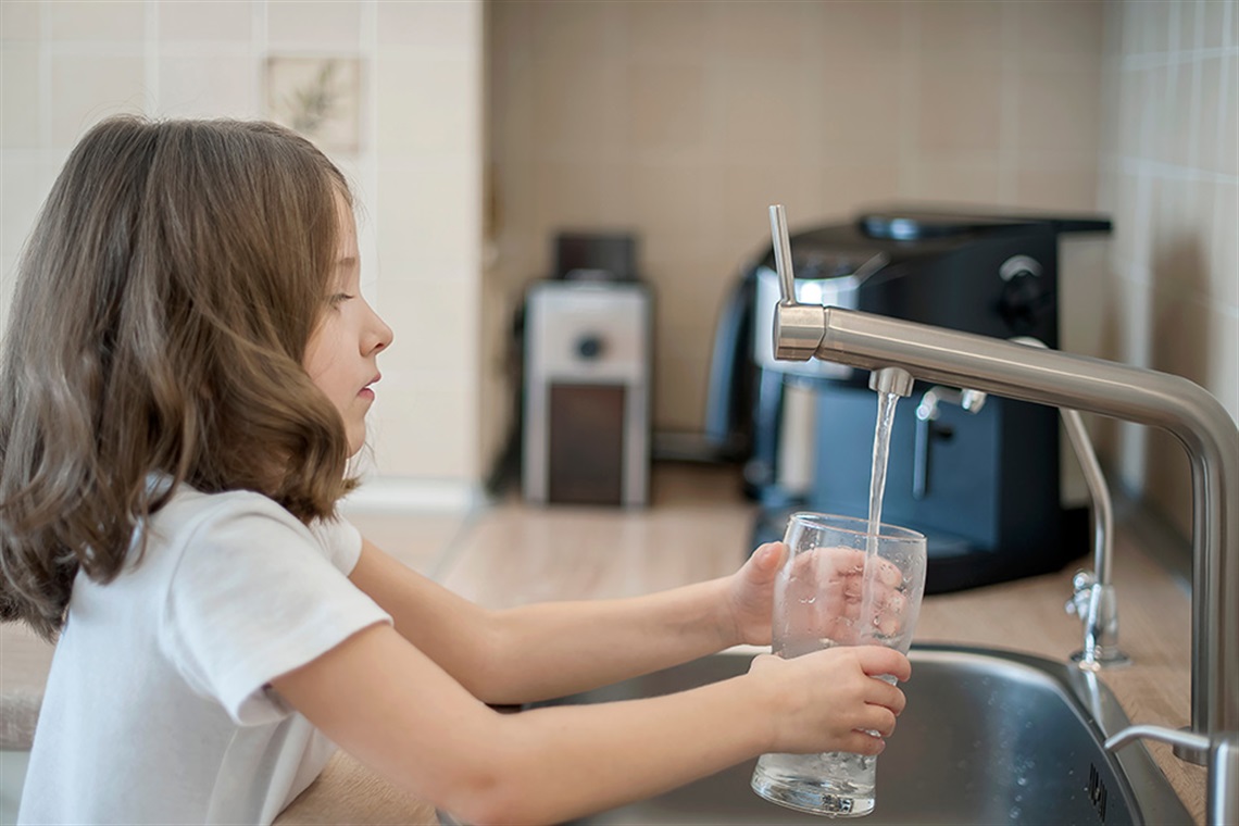 Girl getting a glass of water from a kitchen faucet